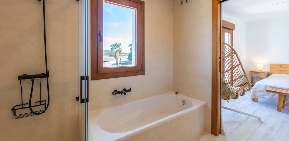 Baño con bañera bajo ventana y carpintería de madera natural.