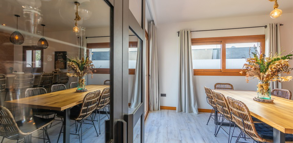 Comedor con mesa de madera, sillas de fibras naturales y ventanal luminoso.