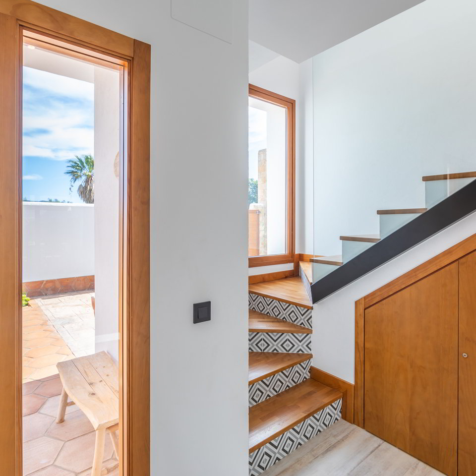 Entrada interior con puerta de madera y escalera con azulejos geométricos.