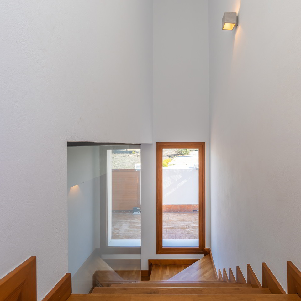 Escalera interior de madera con ventanal vertical y paredes blancas.
