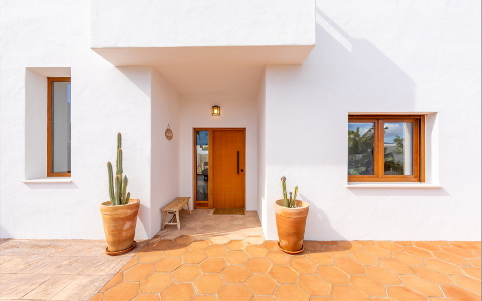 Fachada principal con puerta de madera y macetas de barro.