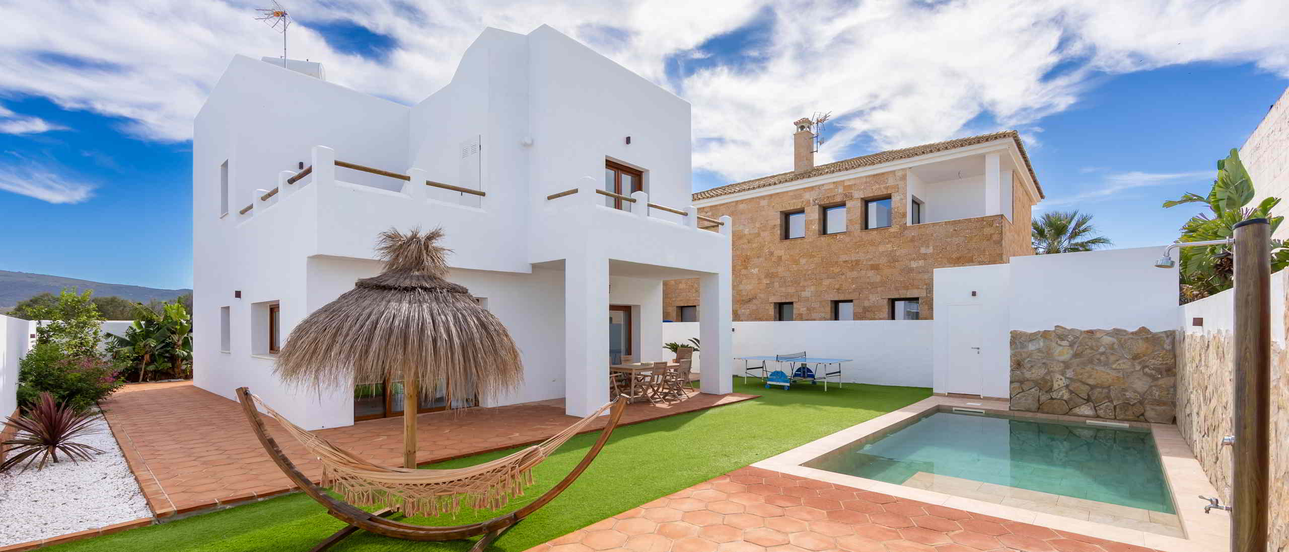 Vivienda blanca con patio privado, piscina y zona ajardinada exterior.
