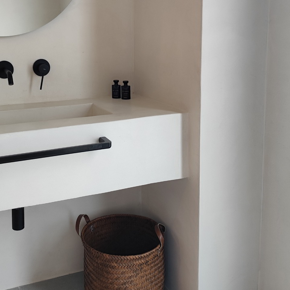 Detalle de lavabo integrado con grifería negra y cesto de fibras naturales.