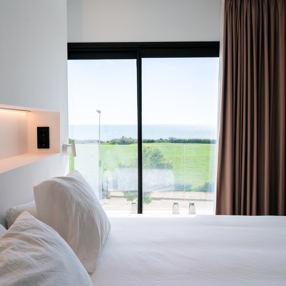 Dormitorio con cama orientada a gran ventanal y vistas abiertas al paisaje costero.