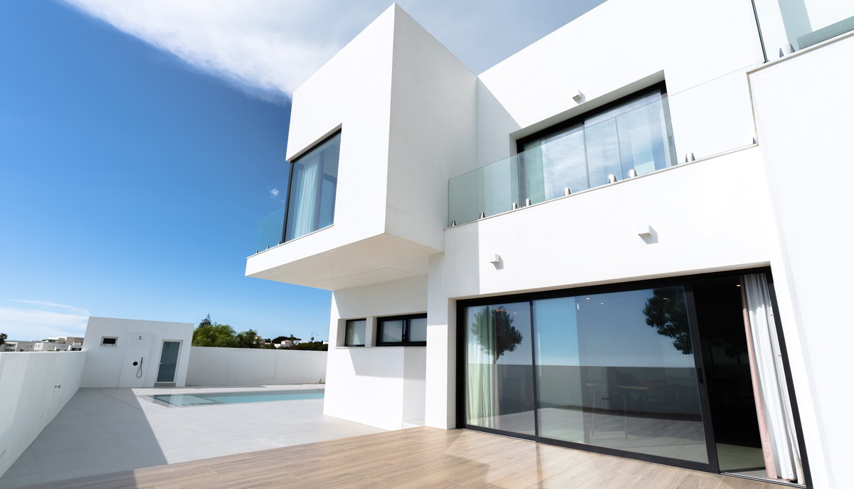Terraza exterior con pavimento de madera, piscina y fachada blanca de vivienda moderna.