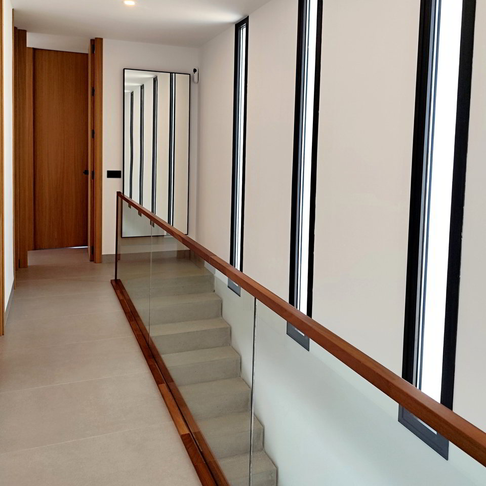 Pasillo interior con ventanas verticales estrechas y barandilla de vidrio.