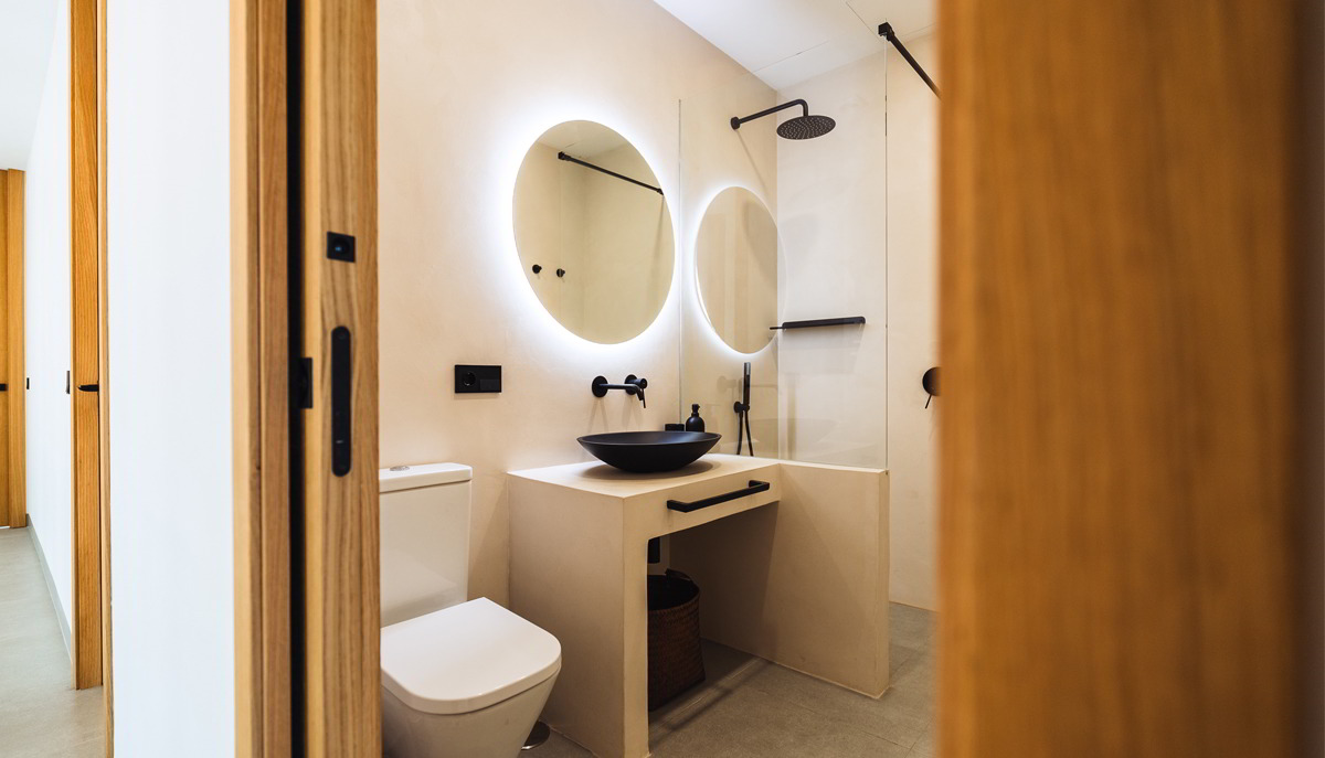 Baño moderno con lavabo integrado, espejo circular retroiluminado y ducha abierta.