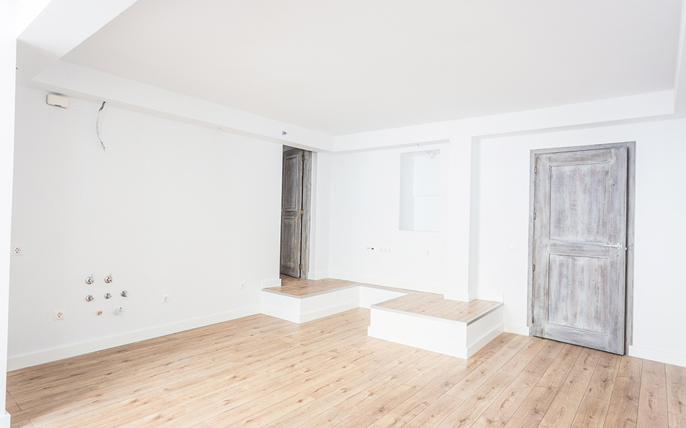 Living room with white walls and wooden floor, with aged wooden door
