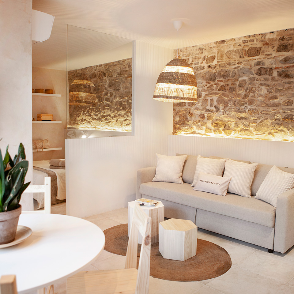 Living room with exposed stone walls, sofa and bedroom at the back separated by a window
