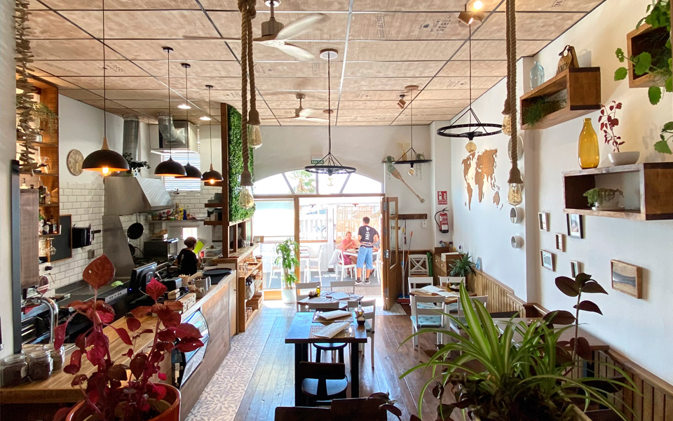 View from inside the Café with the kitchen, bar, tables and glass door with the terrace in the background