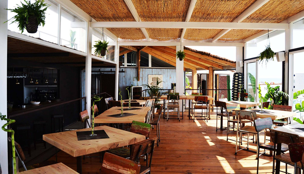 Interior terrace with wooden floors, tables and chairs, with open kitchen