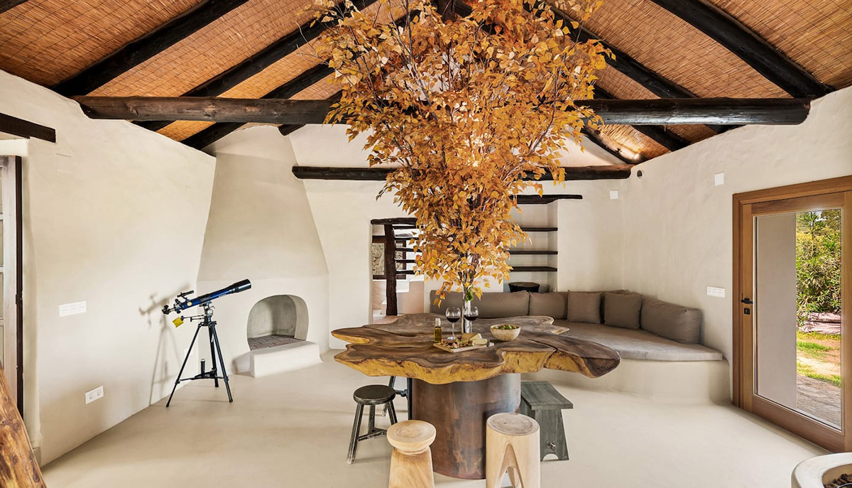 Living room with wooden log table with tree in the middle, round white fireplace, with wood beamed ceiling and heather