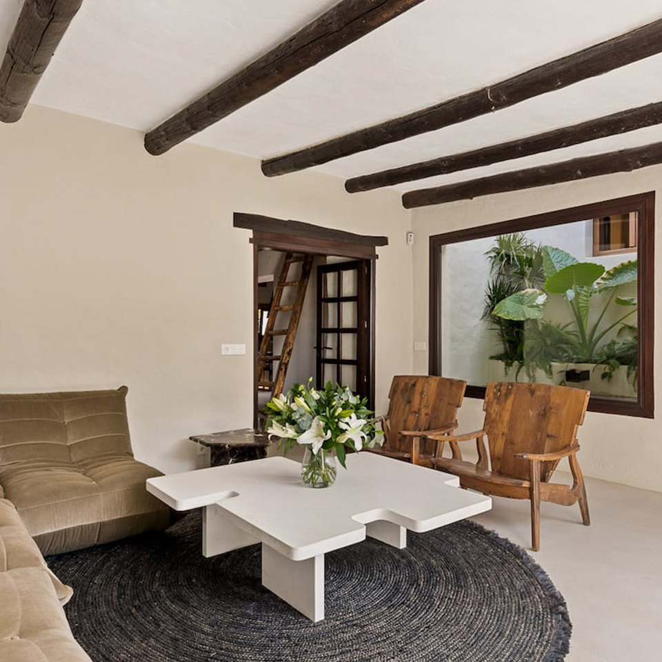 Living room with a white wooden table in the shape of a puzzle, rustic wooden chairs and a window to an interior patio