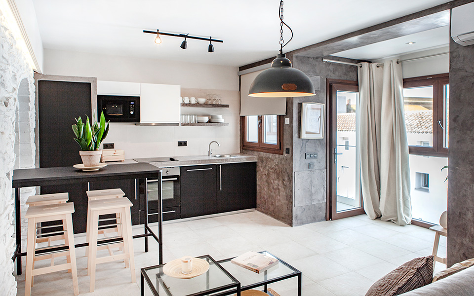 Cocina abierta con muebles oscuros, salón y comedor integrado y ventanales con vistas al patio