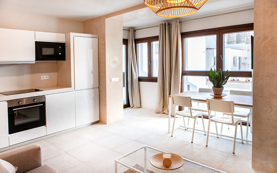 Cocina con muebles blancos, salón y comedor integrado y ventanales con vistas al patio