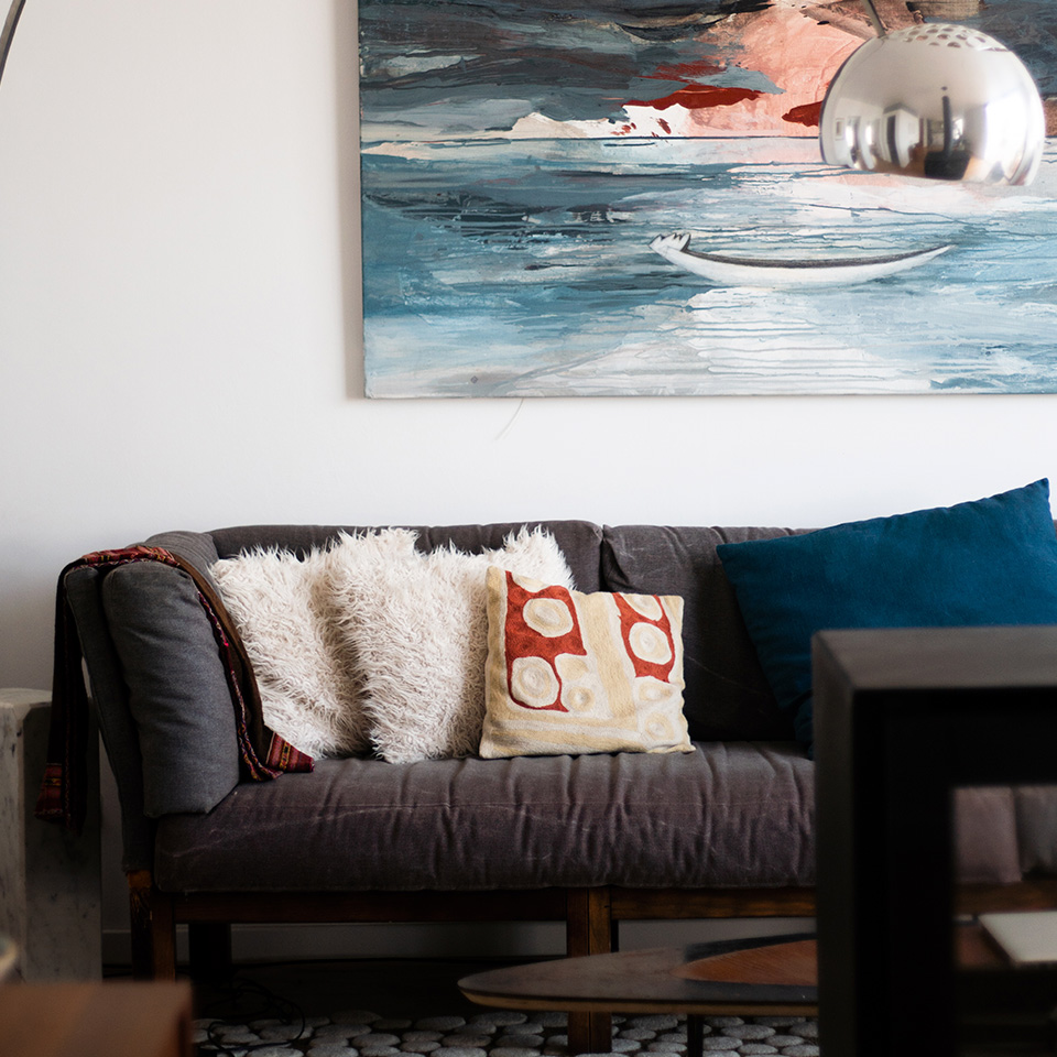 Sofá gris con cojines y cuadro de mar en pared
