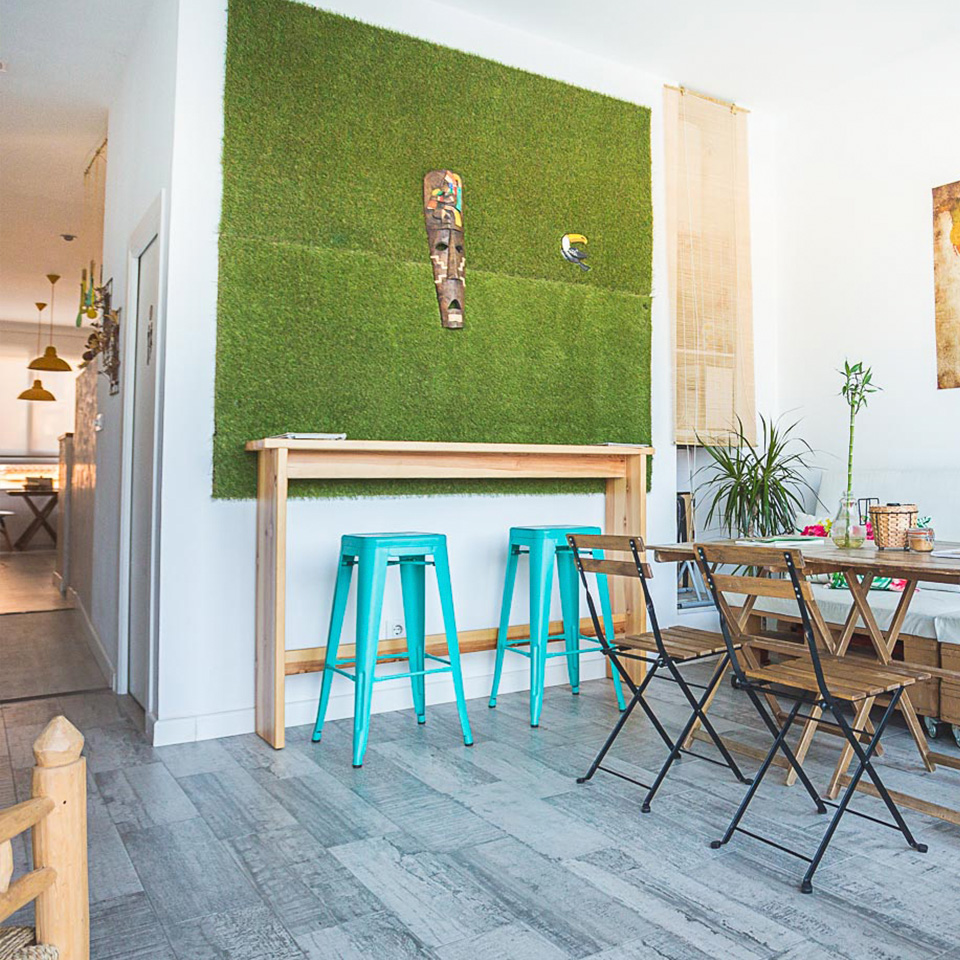 Interior del Café con mesas y sillas de madera, con escultura tiki sobre verde artificial