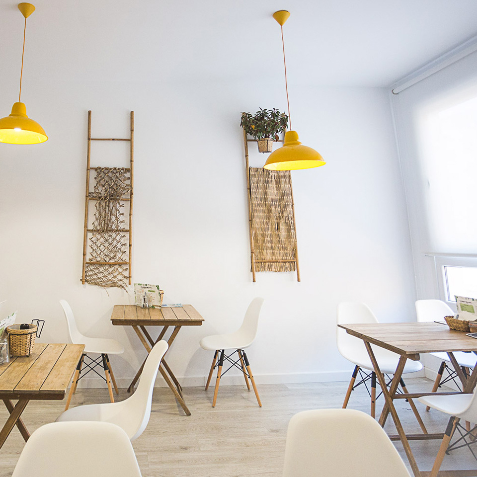 Interior del Café con mesas de madera, sillas blancas y lámparas colgantes amarillas
