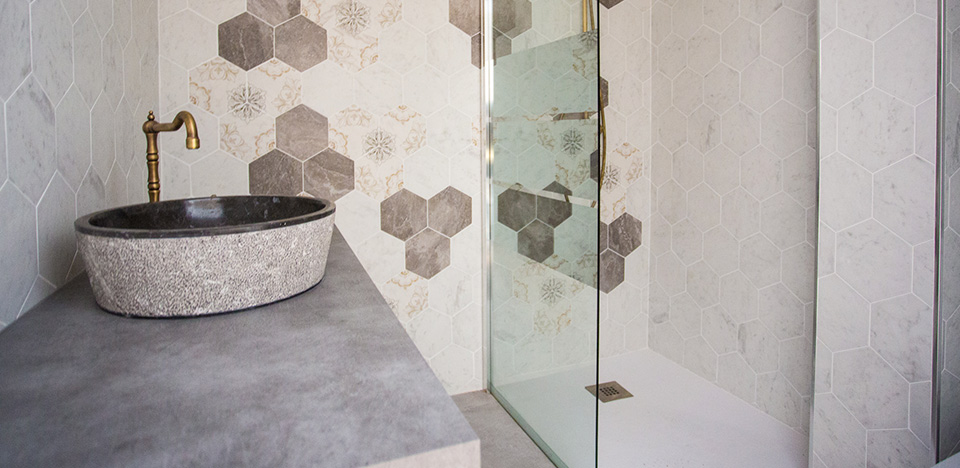 Lavabo de piedra con grifo de metal y ducha abierta con cristalera