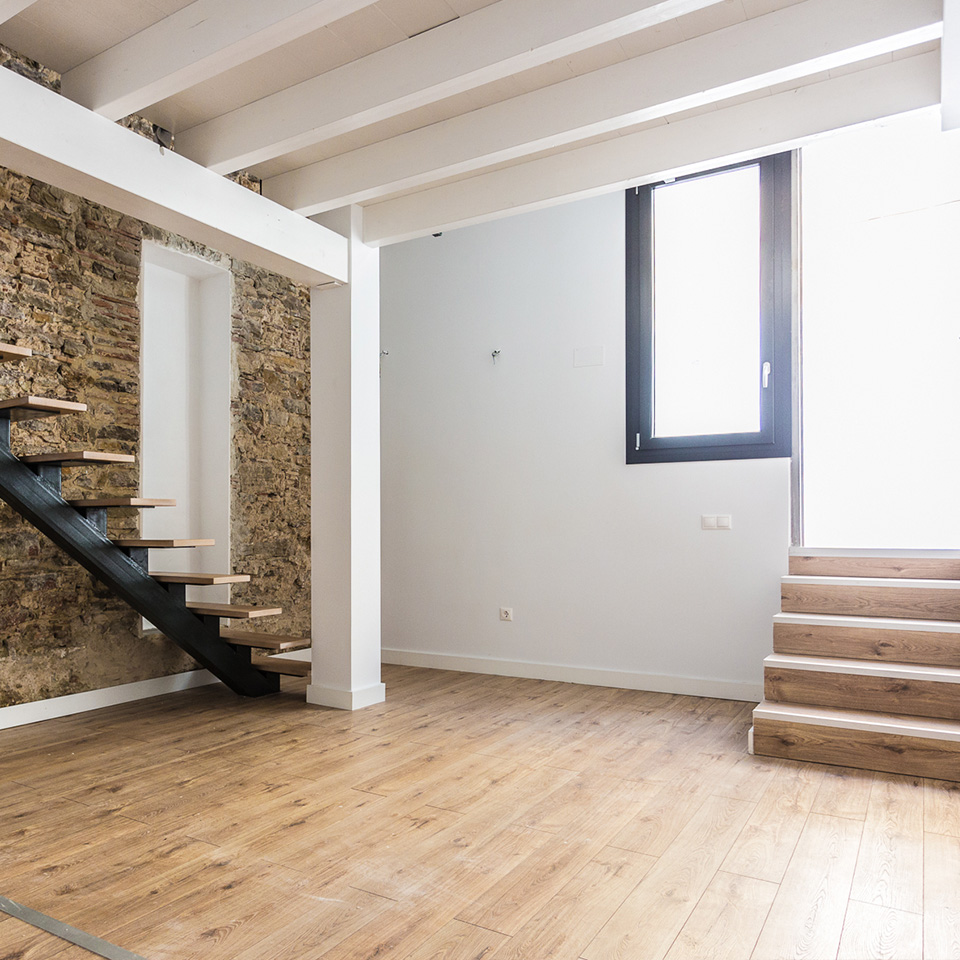 Escaleras de madera de entrada y de subida al primer piso. Suelo de tarima clara.