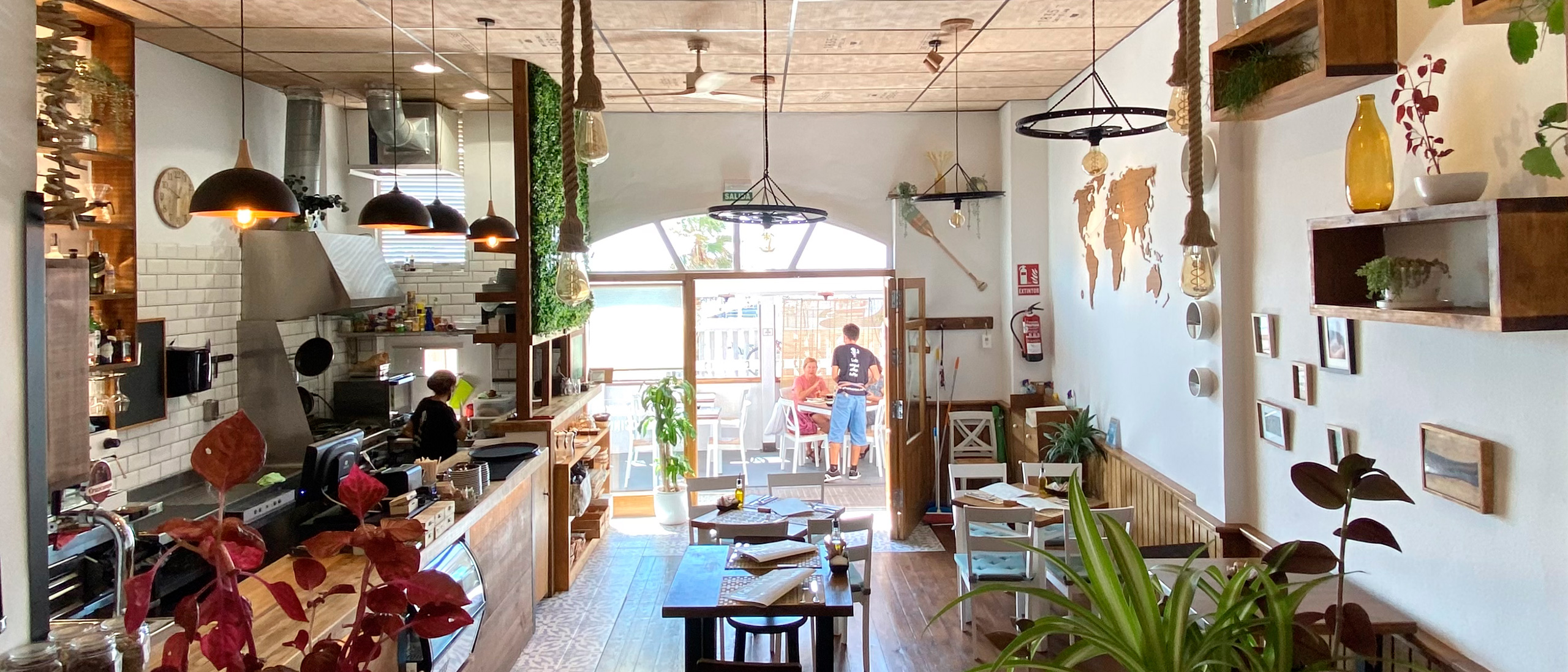 Vista desde el interior del Café con la cocina, barra, mesas y puerta de cristalera con la terraza de fondo