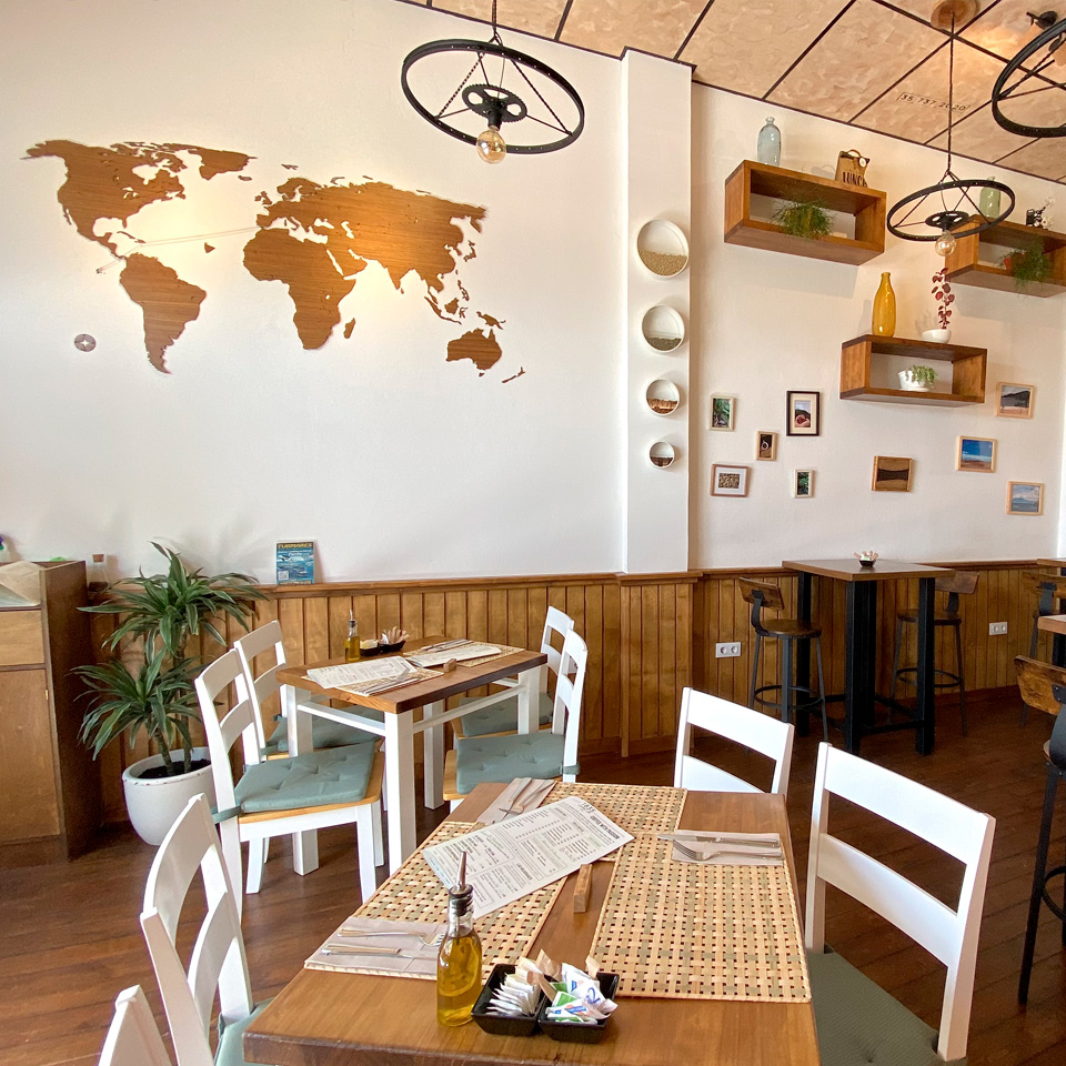Interior del Café con la barra, mesas y sillas; decorado con mapas y estanterías en las paredes
