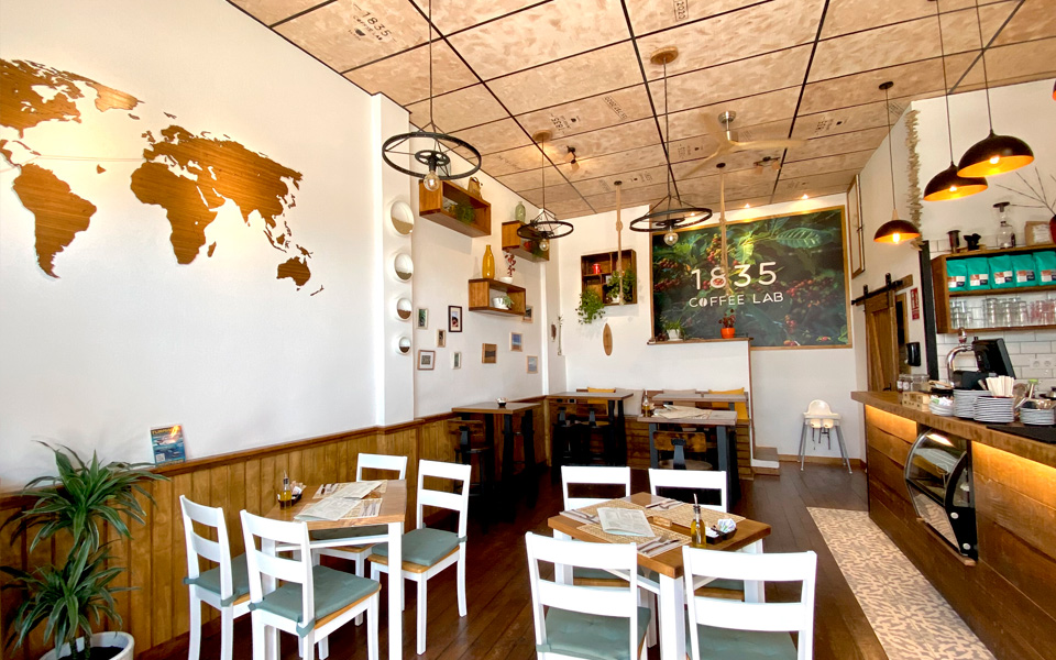 Interior del Café con la barra, mesas y sillas; decorado con mapas y estanterías en las paredes
