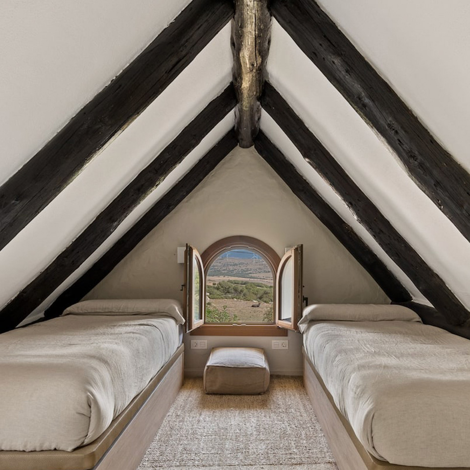 Buhardilla con dos camas individuales, vigas de madera y ventana pequeña redonda