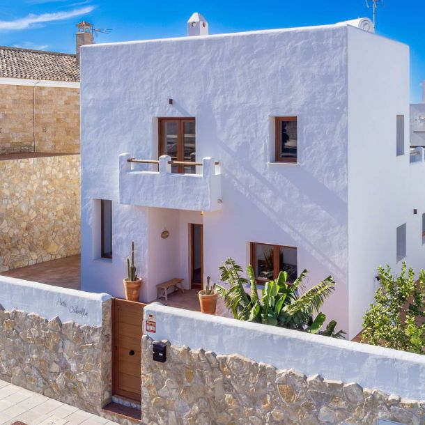 Vista exterior de vivienda unifamiliar blanca con muro de piedra.